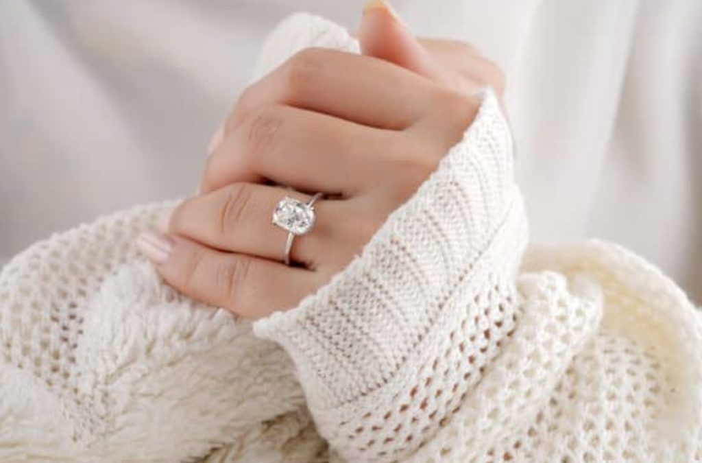 Engagement ring worn on woman's hands snug in a white knitted jumper.