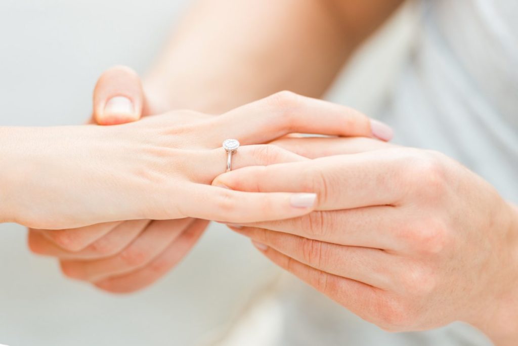 man placing engagement ring on partner's finger