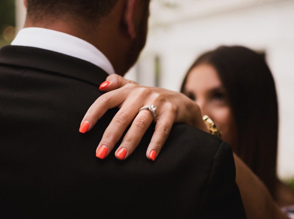 Woman resting engagement ring-wearing hand on her partner's shoulder