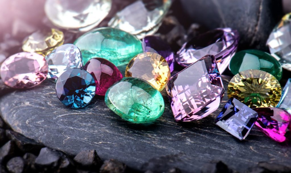 Mix of coloured gemstones sitting on dark rock.