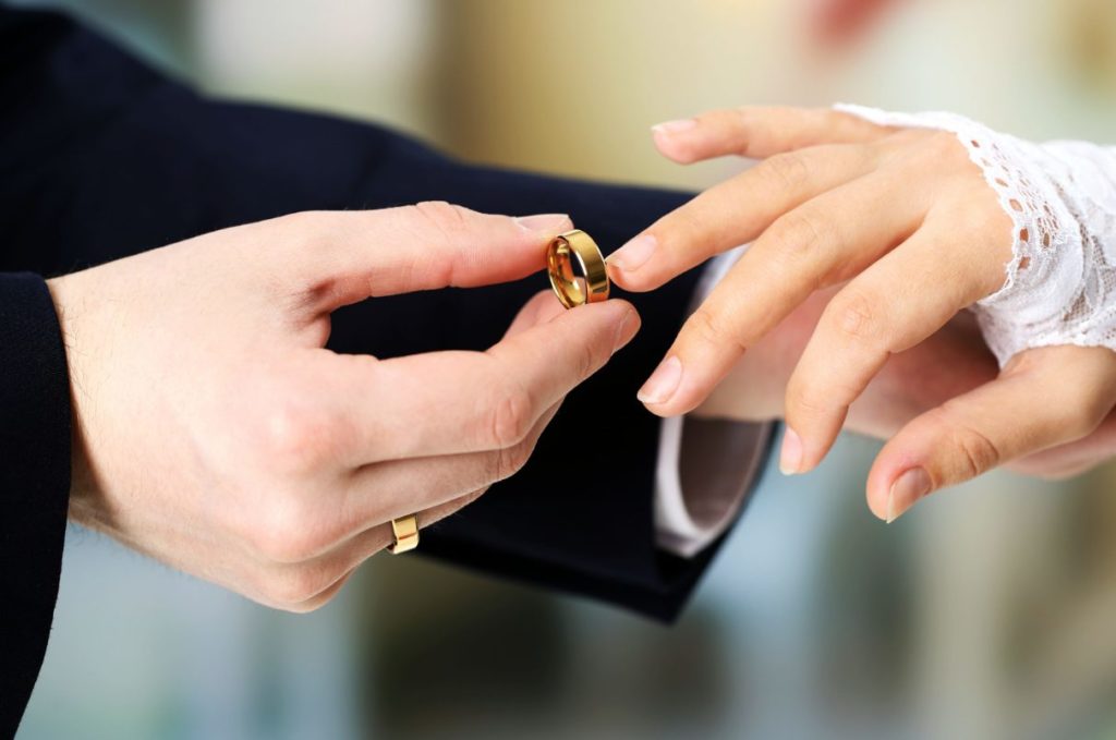 Groom placing wedding ring on bride's finger.