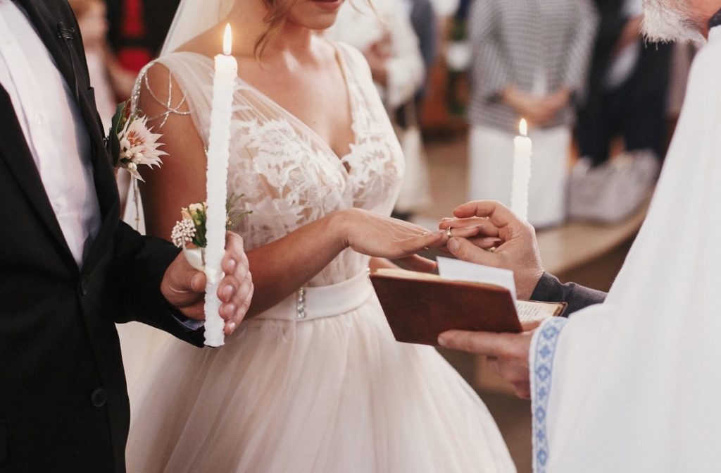 Vicar placing wedding ring on bride's finger as groom holds a candle.